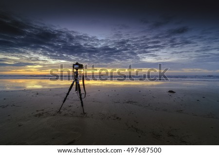 Camera on a tripod taking timelapse by the beach during sunset.