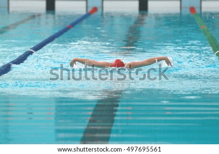 Young swimmer wearing red cap practice butterfly swimming stroke in a swimming pool