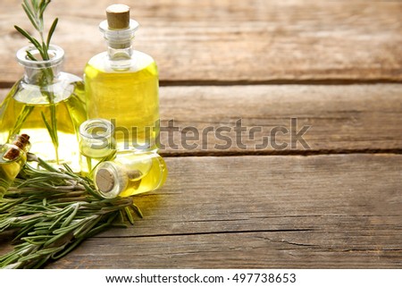 Bottles of coniferous essential oil and rosemary branches on wooden background, close up view
