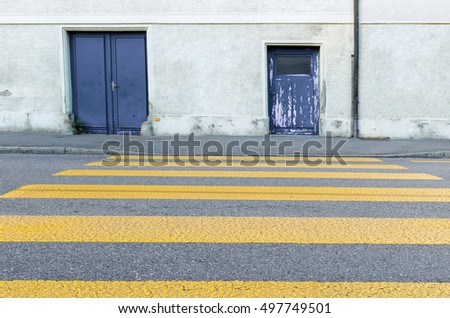 Yellow painted zebra crossing for pedestrians painted on an urban tarmac street looking towards the exterior wall and old grungy doors of a building, low angle view