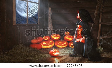 Halloween. child little witch with pumpkin  by the window waiting for a miracle and magic  in old hut