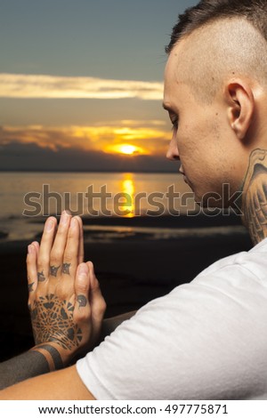 Cropped shot of young tattoo man doing yoga on the beach at sunset. Meditation Pose