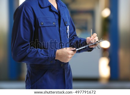 Mechanic in uniform with a clipboard and pen on gas station blurred background Royalty-Free Stock Photo #497791672