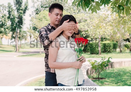 Asian man makes present to his lovely sweetheart. Young man giving a gift. Cheerful young couple man and woman gifts for lover's valentine day. In the park. Filtered image.