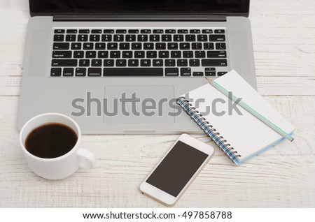 Laptop keyboard, notebook with a pencil, a smartphone and a mug of coffee, top view