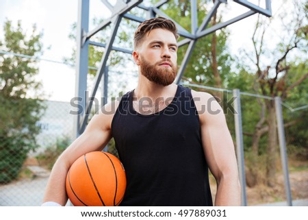 Portrait of a bearded basketball player standing with ball outdoors