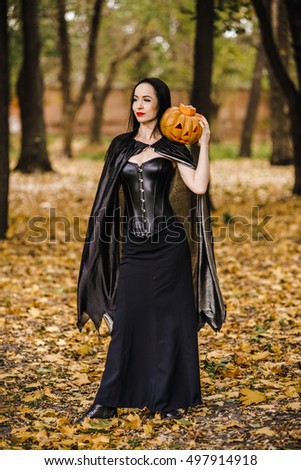 Young witch in the autumn forest. Girl with a pumpkin in black clothes in the park