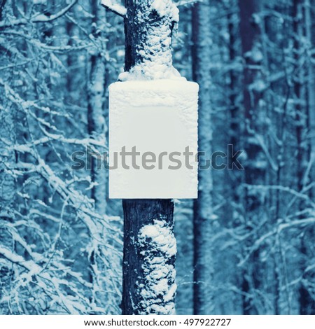 Snowy empty board on trunk of tree winter background 