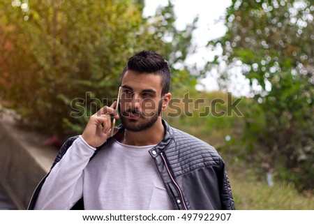 Handsome man talking on the phone outdoors. With leather jacket, sunglasses, a guy with beard. Instagram effect