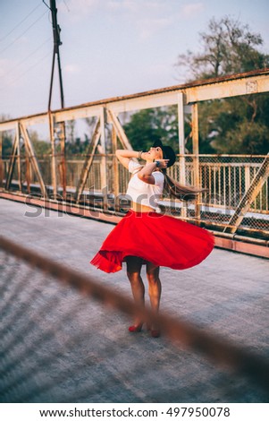 Outdoor lifestyle close up portrait of happy blonde young woman in stylish casual red dress (skirt) and black hat  stay on bridge on the street. Pretty hipster girl having fun and enjoying holidays.