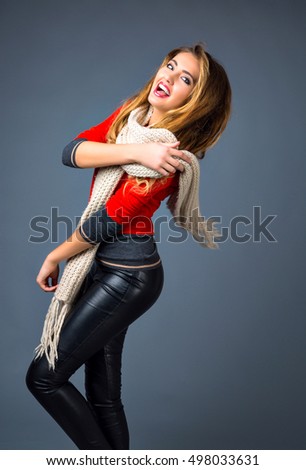 Positive studio fashion lifestyle autumn winter portrait, cheerful blonde woman playing with her scarf, smart casual outfit, sweater, leather pants, happy mood.