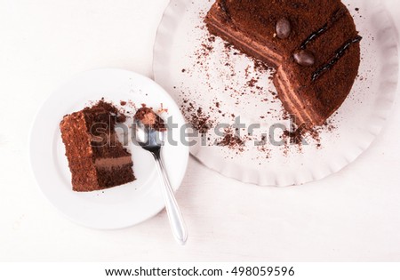 Chocolate cake with cream on a white wooden table. One piece of cake is on the plate, girl eats it, hand in the picture, top view, copy space