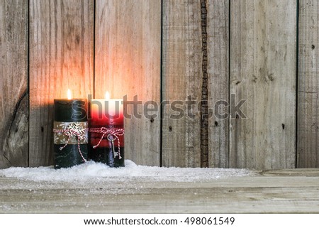 Red and green holiday candles with candy cane striped bow in snow by antique rustic wood background; Christmas and religious background with copy space