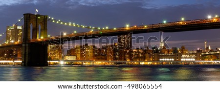Panoramic image of the Brooklyn Bridge illuminated at night with reflections on the East River