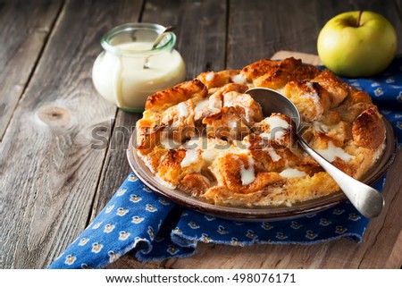 Bread pudding breakfast casserole with apples and vanilla sauce on the old wooden background. Selective focus. Royalty-Free Stock Photo #498076171