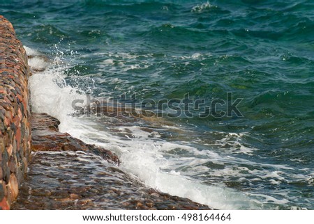 Photo of beautiful clear turquoise sea ocean water surface with ripples and bright splash on stone seascape background, horizontal picture