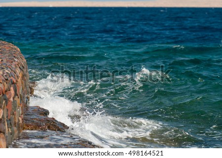 Photo of beautiful clear turquoise sea ocean water surface with ripples and bright splash on stone seascape background, horizontal picture