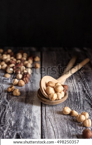 two wooden spoons are filled with roasted hazelnuts. Others hazelnuts are scattered on a wooden base. Vertical picture
