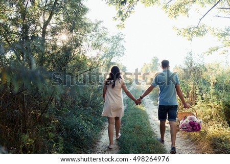 Look from behind at expecting lady and her man with violet basket
