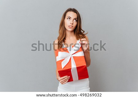 Portrait of a pensive wondered woman holding gift box isolated on a gray background