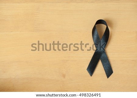 Black awareness ribbon on wooden background. Mourning and melanoma symbol. RIB