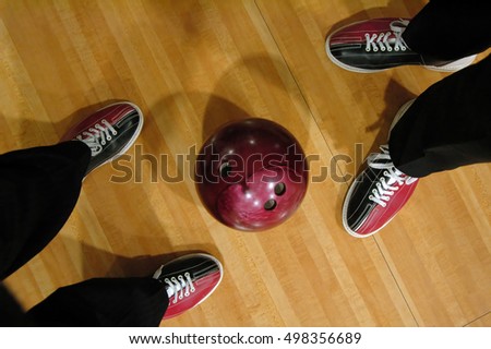 Two men and a bowling ball, two pairs of legs, parquet floor view from above. Flat lay
