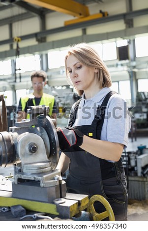 Mature female worker working on machinery with colleague in background at factory