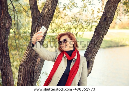 Beautiful red-haired woman doing selfie in autumn park.