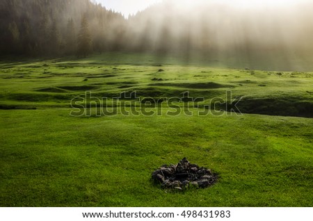 Outdoors background.Camping in the meadow.Unlit camp fireplace with ashes and stones.Bright sunrise over green field.Camp Fire.