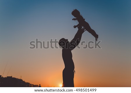 Back side view silhouettes of joyful father and little baby playing at sunset background. Love, book cover idea design