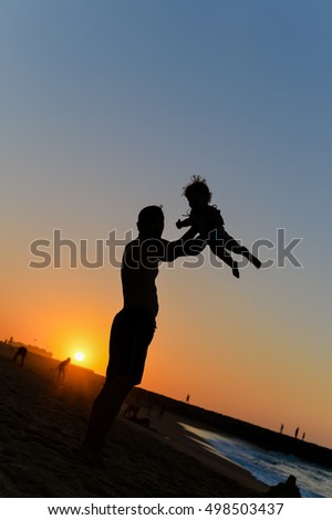 Back side view silhouettes of joyful father and little baby playing at sunset background. Love, book cover idea design