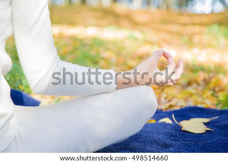 Woman wearing white clothes relaxing and practicing yoga in the park atmosphere, where sunlight plays with shadows. Focus point on the hand.
