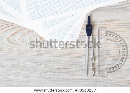 Layout with compass, protractor and graph paper on wooden surface in top view. Workplace of draftsman, architect, constructor or designer. Engineering work. Measurement. Tools for drawing.