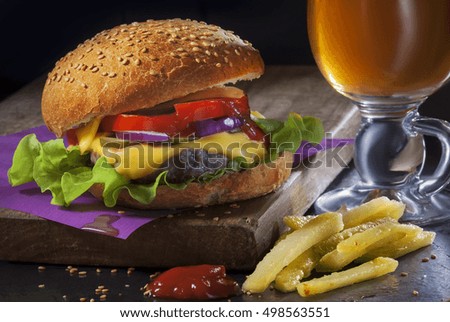 Fresh home-made hamburger served on wood with fries and drink over dark background