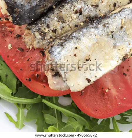 Sardines with cracked black pepper on a bed of sliced tomato and green rocket leaves