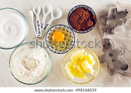 Ingredients for baking on a white marble table : flour, eggs, cocoa powder, sugar, butter and measuring spoons, molds