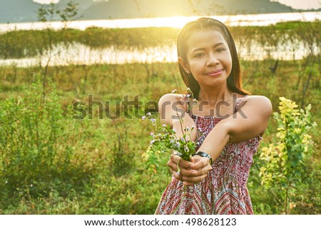 Asian beautiful woman is smiling and giving a bouquet of flowers. A beautiful woman in rim light. Picture in warm tone and retro style.