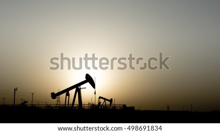 Silhouette of crude oil pump in oil field at sunset