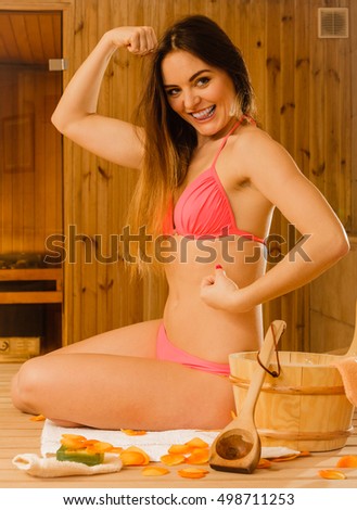 Portrait of young woman relaxing in wooden finnish sauna showing off muscles. Attractive girl in bikini resting. Spa wellbeing pleasure.