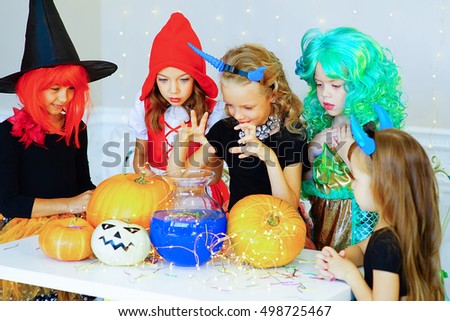 Happy group of children in costumes during Halloween party playing around the table with pumpkins and bottle of potion