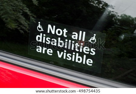 Prejudice, Not all disabilities are visible sign. A sticker with white text and wheelchair symbols stuck to the inside of a car window. 