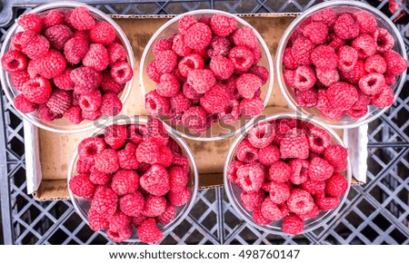 ripe red raspberries in plastic glasses against black grid, concept of veganism, organic sweet juicy natural food, top view, fruit salad, raspberries texture as background, high quality resolution