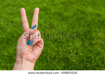 Women hold two fingers on green grass background texture