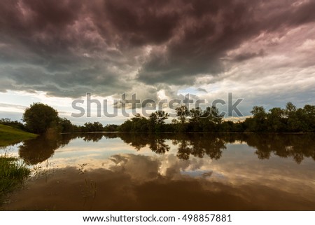 Ominous stormy sky over natural lake, with dark red and grey cumulus clouds