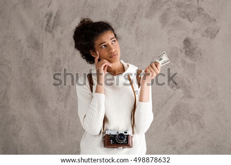 African female photograph thinking, holding money over beige background.