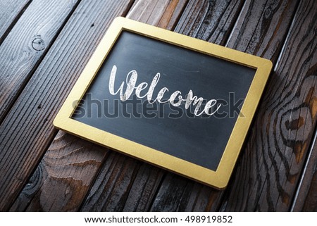 Welcome Sign Written In Chalk On Chalkboard On Rustic Vintage Wood Background. Selective Focus.