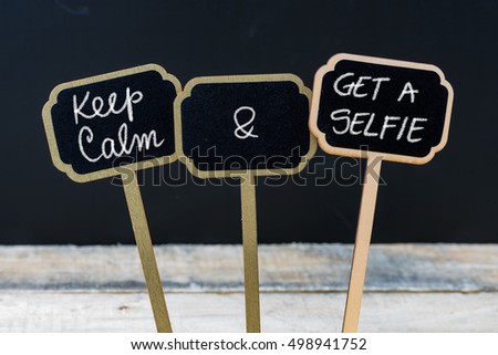 Keep Calm and Get A Selfie message written with chalk on mini blackboard labels, defocused chalkboard and wooden table in background. Fun and humor concept