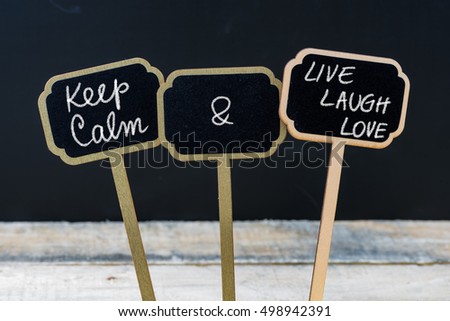 Keep Calm and Live Laugh Love message written with chalk on mini blackboard labels, defocused chalkboard and wooden table in background. Fun and humor concept