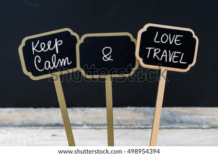 Keep Calm and Love Travel message written with chalk on mini blackboard labels, defocused chalkboard and wooden table in background. Fun and humor concept