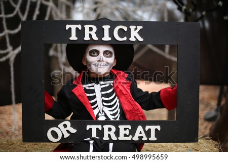 Boy in a Halloween costume of skeleton with hat and smocking holds a frame a "Trick or treat" title.

